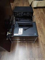 Photo showing two Realistic brand amplifiers stacked on top of an IBM ThinkPad laptop, all placed on a chrome wire rack stand with wooden floor background.