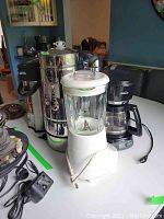 Photo showing both the Cuisinart blender with glass jar and Sunbeam coffee maker side by side on a white surface, cords visible.