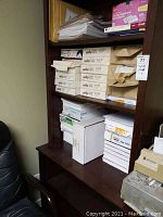 Wooden shelving unit with stacked paper reams and several boxes of envelopes.