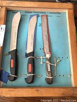 Three Premiere branded cutting tools mounted on a blue board with wooden frame. Each tool has a black handle with orange labels and steel blades.