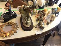 Wide shot of lot showing multiple elephant figurines, a decorative sunburst mirror, and a golden pig figurine arranged on a wooden table.