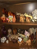 Photo showing two shelves filled with around thirty-five elephant figurines in wood, glass, metal, and stone materials.