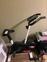 Exercise bike from left side showing seat, handlebars, and some items beside it.