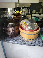 Glass baking dishes of varying sizes stacked, wooden churning pot with metal bands and blender on a kitchen counter