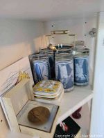 Shelf with six blue and white glasses with classical figures next to the small white trinket box with decorative lid