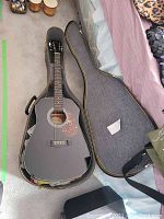 Photo showing black Hondo acoustic guitar inside an open black hard case with gray interior, placed on carpeted floor.