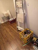 Step ladder leaning against the wall with a yellow Pepsi crate holding tape and taping tools on the floor next to it, and a red crate with additional items in the background.
