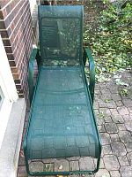 One of the green metal and mesh lawn chairs photographed upright on a brick patio with foliage in background, showing mesh seat and backrest, curved armrests, and metal frame construction.