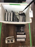 Plastic tub labeled 'Assorted Pens' containing multiple boxed pens and loose pencils