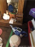 Photo of a blue and white elephant-shaped ceramic pitcher, pale pink elephant-shaped plant stand, and various small animal figurines on a wooden surface near a carved wooden post.