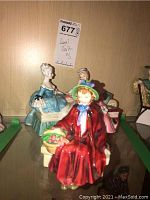 Three Royal Doulton figurines on shelf, including Linda in red coat and two-lady bench figurine