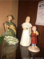 Three Royal Doulton figurines displayed side by side on a glass shelf under a wooden background.