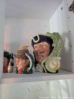 Two Royal Doulton Toby jugs including one with navy blue hat and green crocodile spout and another with brown hat and spout resembling a duck head.