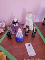 Lot of Royal Doulton porcelain figurines and a purple glass elephant on a wood surface with green tape markings around.