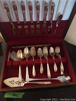 Full set of silver plate flatware displayed in a red-lined storage box showing utensils held in slots on the lid and base.