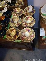 Six teacup and saucer pairs displayed on wooden surface in front of mirror