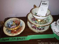 Three tea cup and saucer sets displayed on a surface, two stacked and one set separate