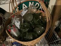 Woven basket filled with assorted clear and green glass cups and tumblers, some have printed designs