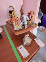 Wide view of all Winnie the Pooh character statues including Pooh, Tigger (3), Eeyore, Piglet, Elmo, and glass trinket box on wooden shelf.