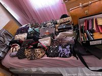 Full view of bed covered with assorted vintage handbags and purses, with a box of clutch wallets on the side.