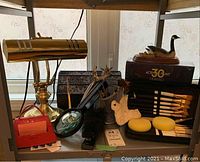Brass-colored desk lamp, magnifying glass, small stationery items including pens, a stapler, small decorative wooden duck, and unopened acrylic paint set