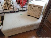 White leather-like bench with storage ottoman placed on top, showing the bench's smooth surface with scruff marks and brown wood floor underneath.