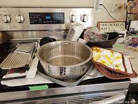 Cast iron pans, colander, baking tray, kitchen mitts, and assorted kitchen items on stove and counter