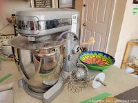 Front and side view of mixer on countertop with bowl and attachments visible
