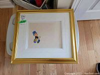 Full shot of framed Disney animation cel showing Jiminy Cricket character in gold frame with white matting.