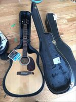 Full view of acoustic guitar inside open hard case showing guitar body, neck, and control knobs.