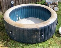 Full view of inflated round hot tub on grass, dark blue vinyl exterior with dirt marks
