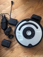 iRobot Roomba Model 561 vacuum cleaner with charger, batteries, and wheel accessory on wood floor.