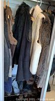 Closet hanging with over 10 jackets and vests in neutral colors including black, white, and brown with faux fur texture details.