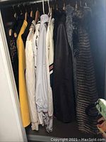 Nine women's jackets and vests hanging on a closet rod showing variety of colors and styles, including yellow, white, black, faux fur, and leather or leather-like material.