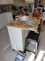 Front and one side view of the white wood kitchen island cabinet on castors with natural wood countertop and kitchenware on top.