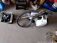 Full view of vacuum, hose, wand and basket of attachments on garage floor