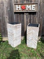 Two tall wooden planter boxes on grass by a wooden fence with 'HOME' sign above them.