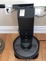 Front view of docking station with Roomba docked, wall outlet and baseboard visible