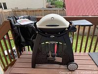 Full view of grill on porch with cover draped on left and manual on side shelf