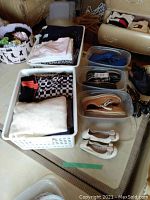 Photo of plastic storage totes filled with folded women's tops and clothing, along with shoes lined up beside them