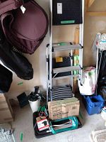 Photo showing two aluminum step ladders, waste bags, garden tools, black plastic bench, and various gardening equipment arranged on the floor and wall.