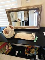 Full view of gold-framed beveled mirror with UGG shearling ear muffs and cream gloves on table.