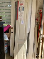 Stack of white bifold doors with visible hardware holes and protective wrapping on edges.