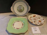 Photo of three antique plates on table showing various floral and scenic designs.