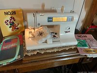 Full view of machine on tabletop with sample embroidered fabric, design cards No.28 and No.44, large frame packaging visible