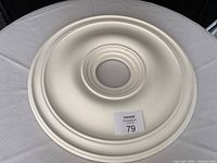 White round ceiling medallion on table, showcasing the smooth finish and central hole for lighting fixture.
