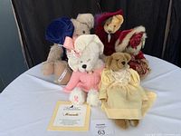 Photo showing 5 collectible teddy bears in vintage-style clothing on a white table against black background, with certificate and auction labels visible.