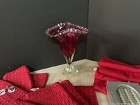 Photo of fluted cranberry glass vase with clear pedestal base surrounded by red cloth napkins.