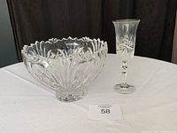 Photo of crystal bowl and champagne flute side by side on white tablecloth and dark backdrop
