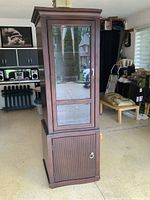 Closed cabinet showing dark wood finish and vertical rectangular shape with upper glass door and lower wood door.
